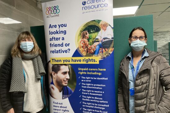 Carers' Resource staff wearing masks in front of a Carers Rights Day banner inside a mosque